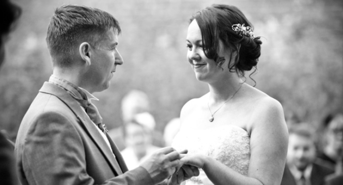 A man is putting a wedding ring on a woman 's finger.