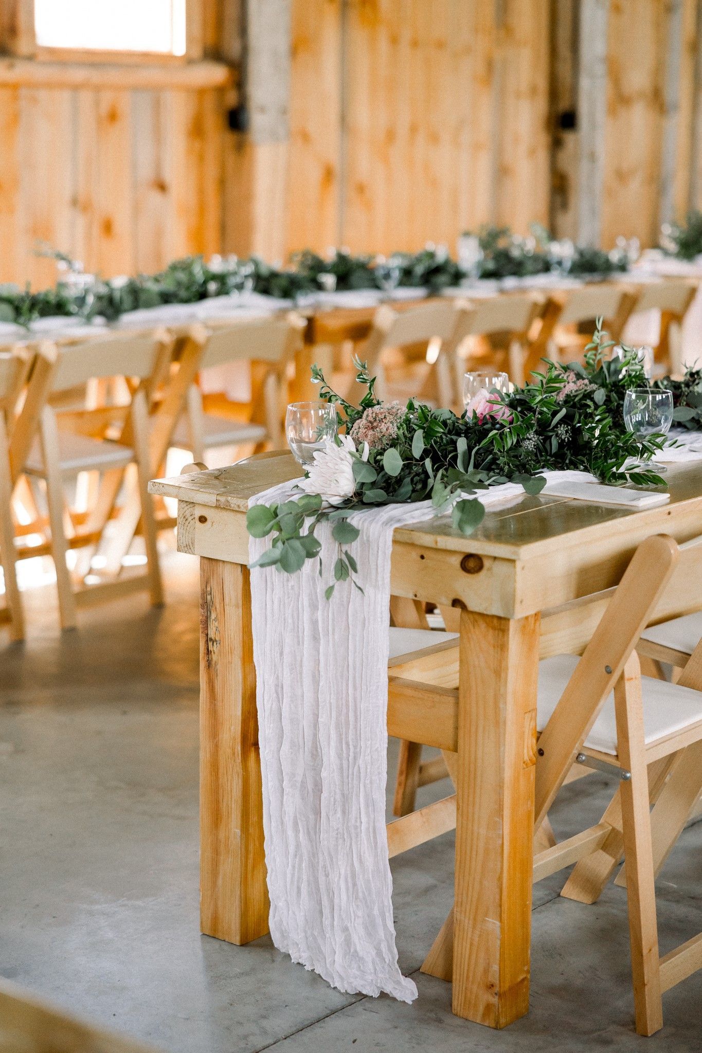 up close details shot of a wedding reception table in the isham family farm events barn with linen runners and eucalyptus leaves