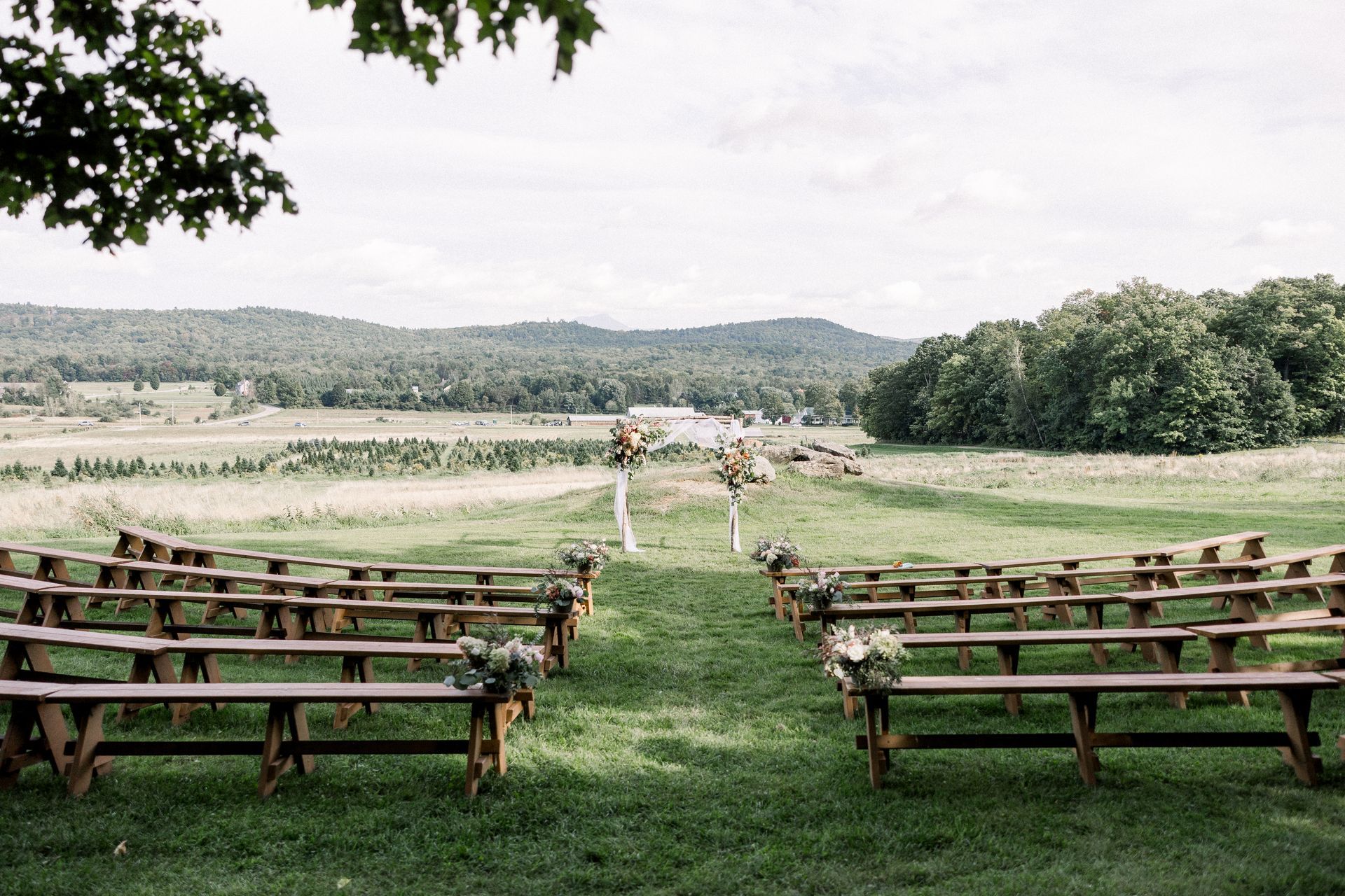 benches decorated and facing the floral arch of a wedding set up at isham family farm in vermont