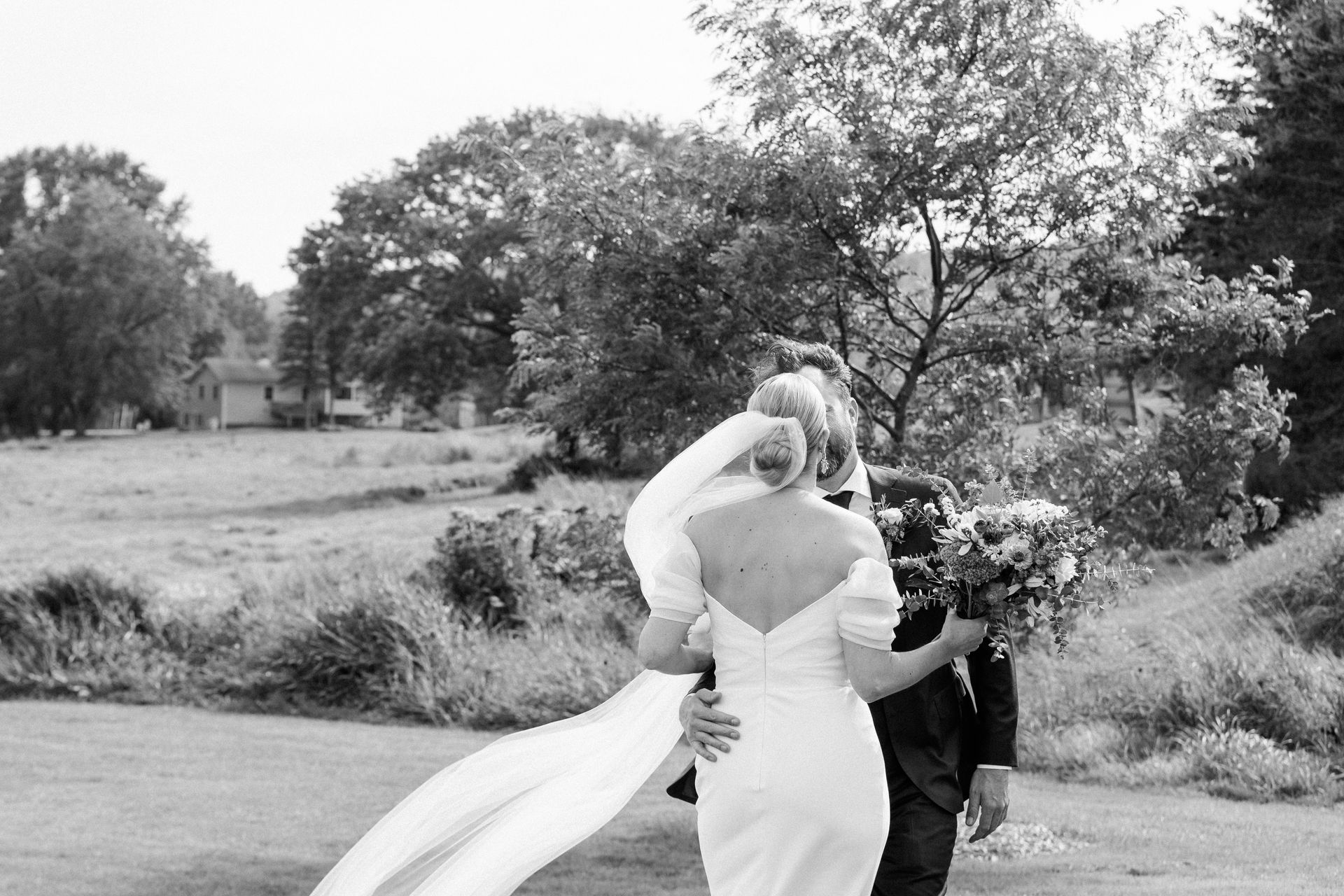 black and white shot of just married couple kidding from the back in front of the trees at isham family farm in vermont