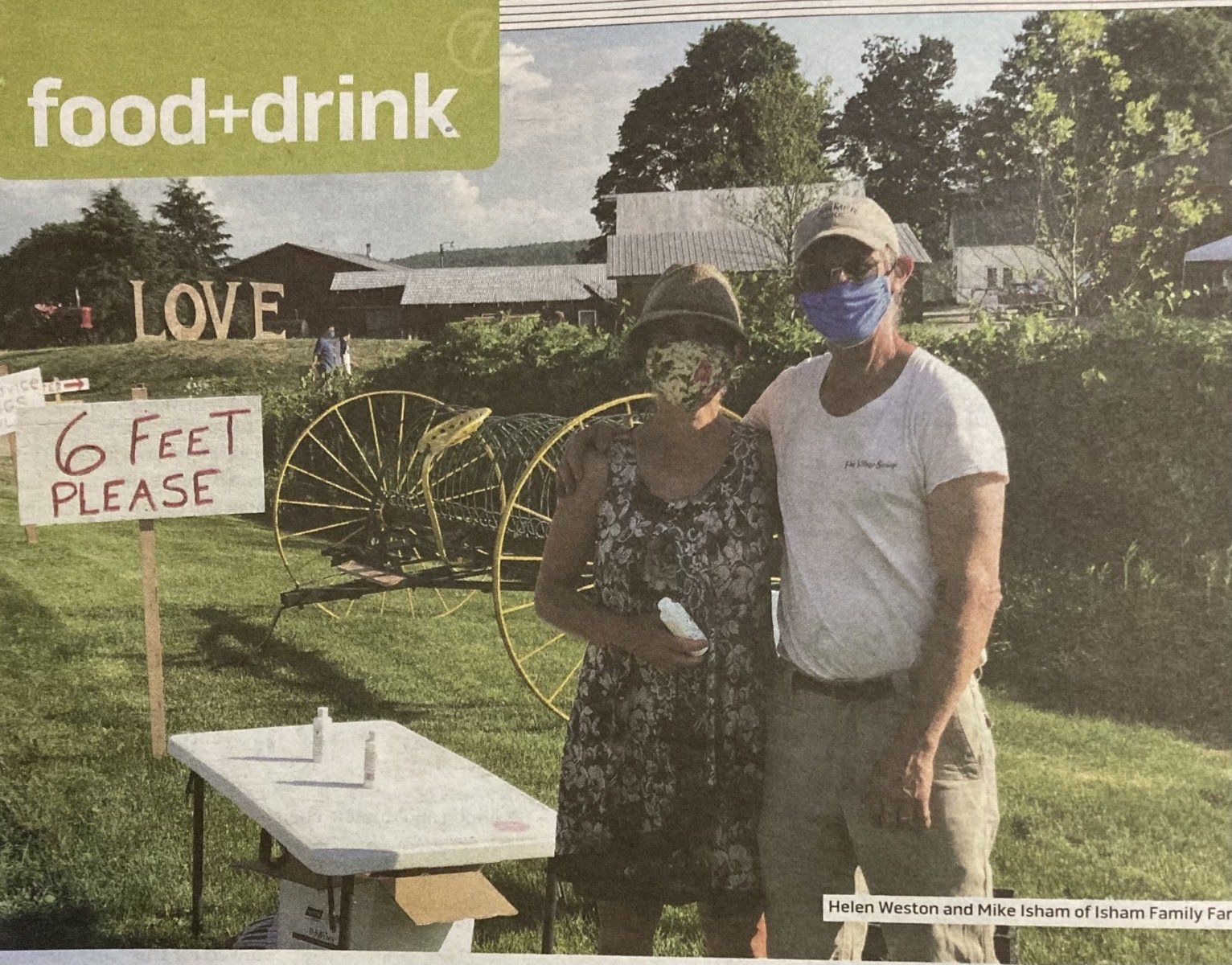 Helen and David Isham wearing masks in front of a social distancing sign during the covid 19 period.