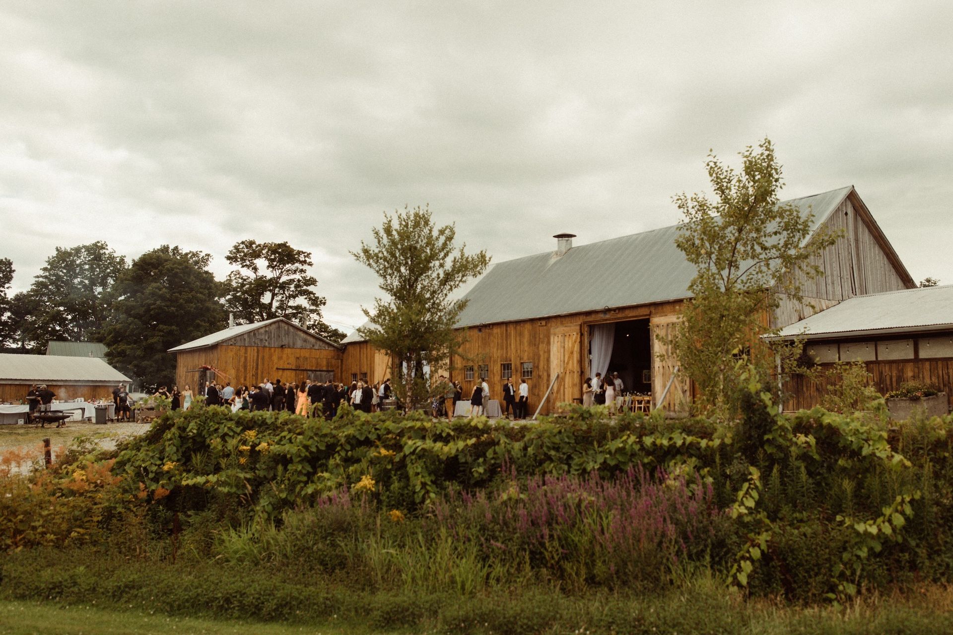 moody shot of the isham family farm events barn on an overcast day as guests walk in for a wedding reception