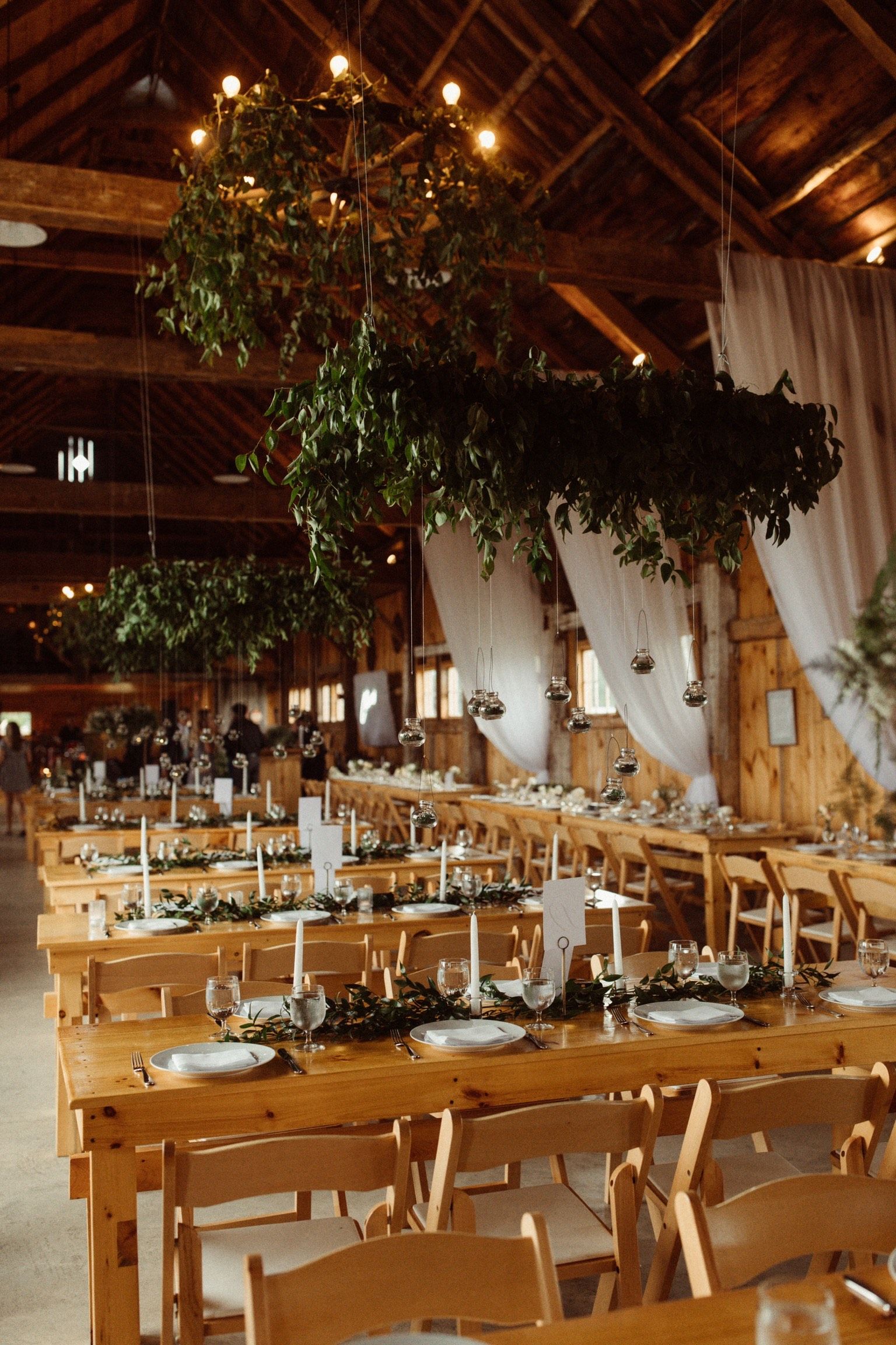 wedding details shot of reception dining room with greenery hanging from the ceiling over the tables.