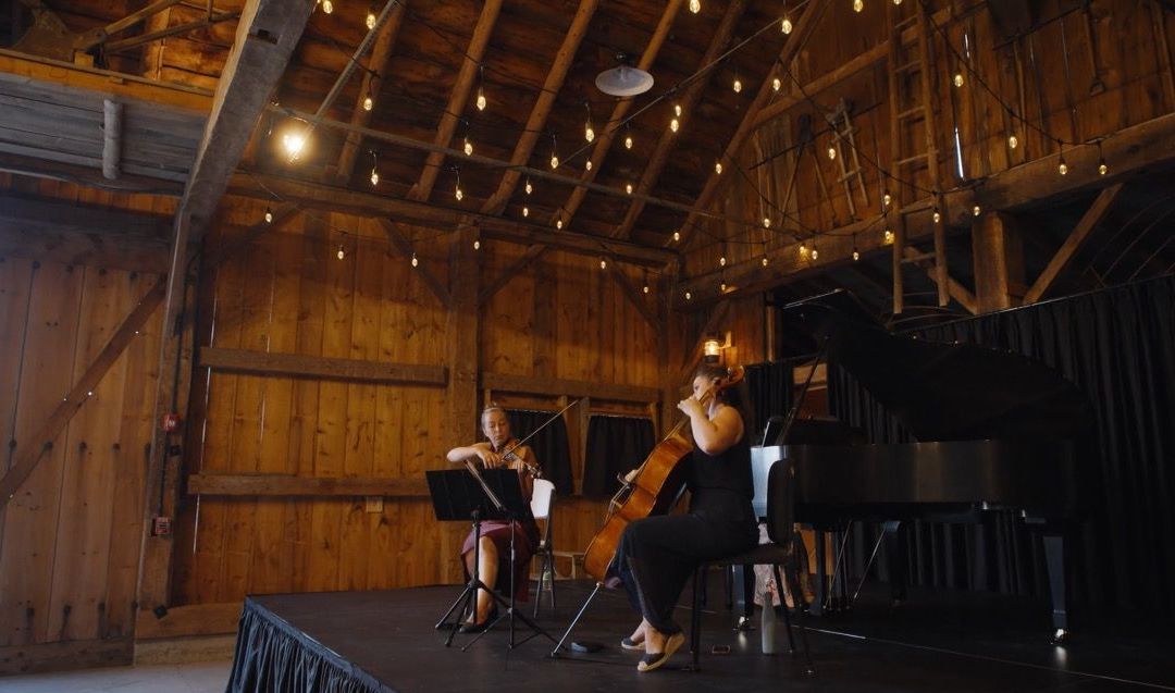 cello and violinist performing on stage inside the events barn at isham family farm 