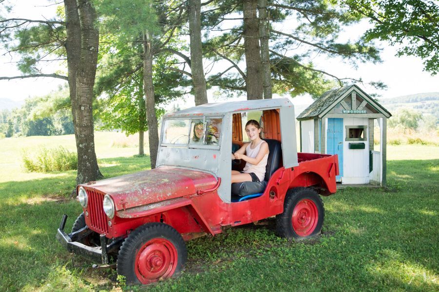 girl driving old converted jeep truck with no doors around isham family farm in vermont
