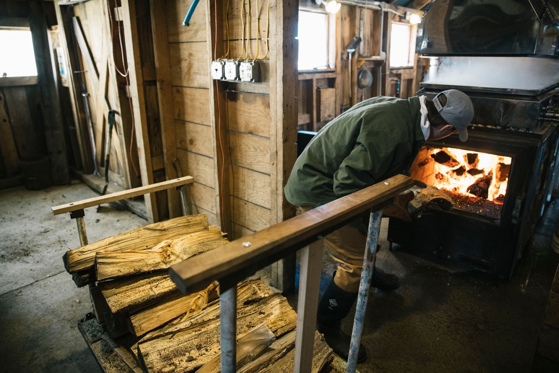 Sugarmaker stoking the wood-fired evaporator inside the sugarhouse at Isham Family Farm during maple syrup season in Vermont.