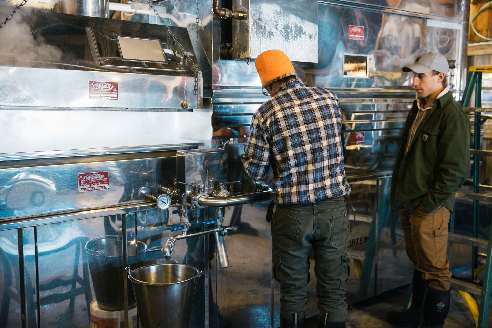 Two sugarmakers at Isham Family Farm monitoring stainless steel evaporator during maple syrup production in Vermont.