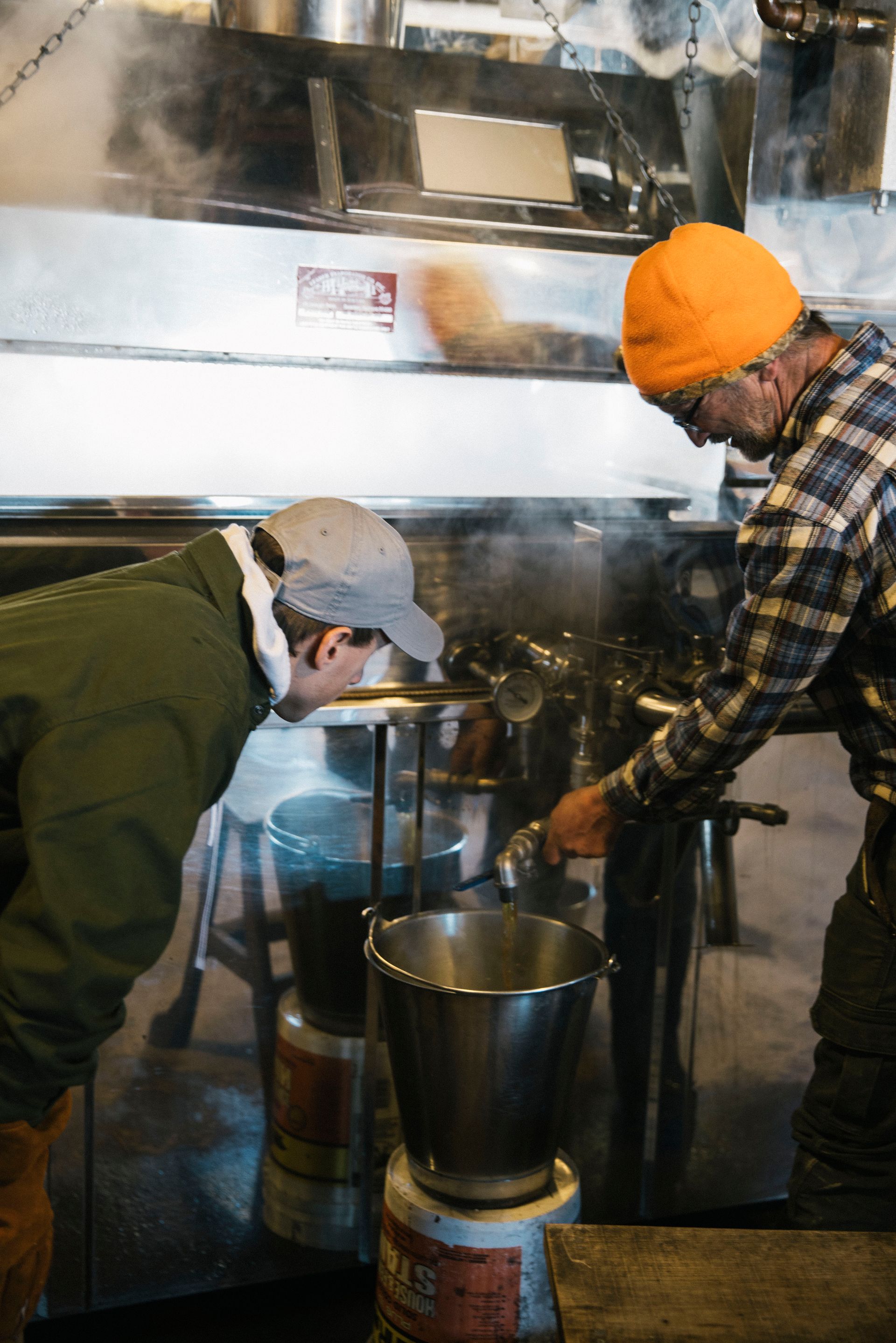 Pouring fresh Vermont maple syrup from the evaporator into a stainless steel pail at Isham Family Farm sugarhouse.