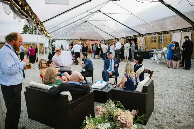 candid shot of wedding attendees enjoying a cocktail hour in the isham family farm outdoor event tents.