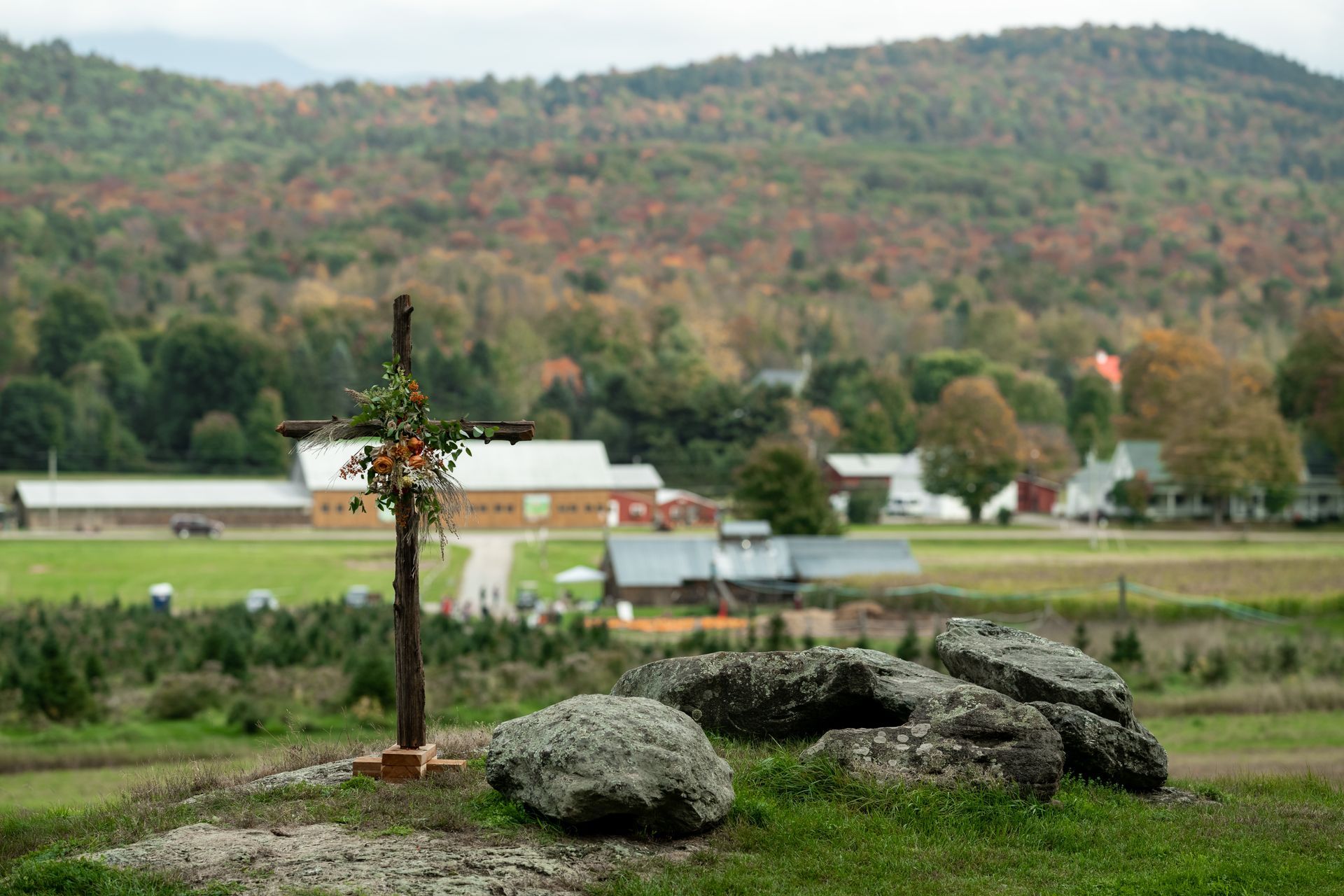 A wooden cross decorated with flowers standing atop a hill with rocks ahead of a wedding ceremony at isham family farm