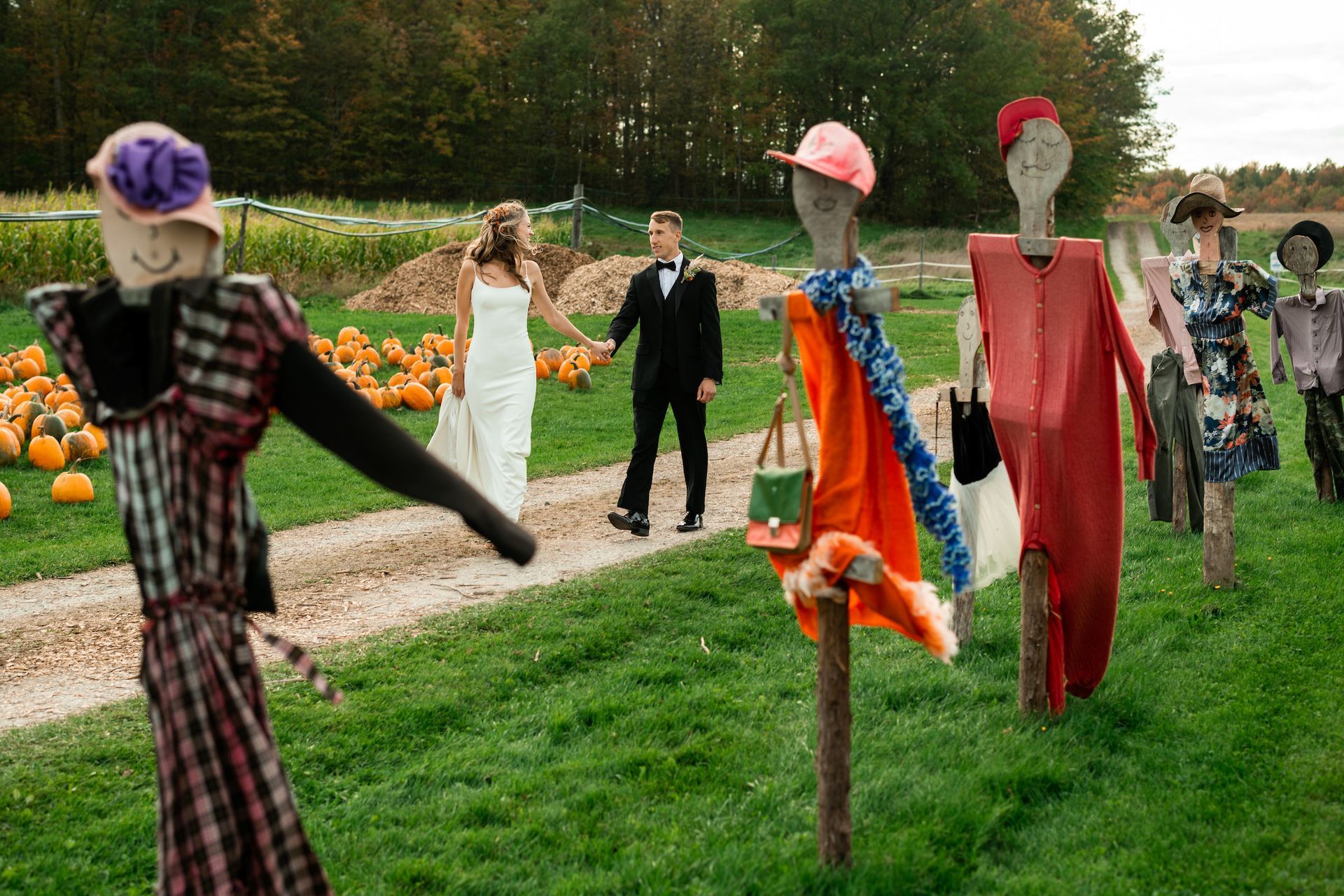 a bride and groom holding hands walking a path punctuated by dressed scare crows from isham family farm fall festival