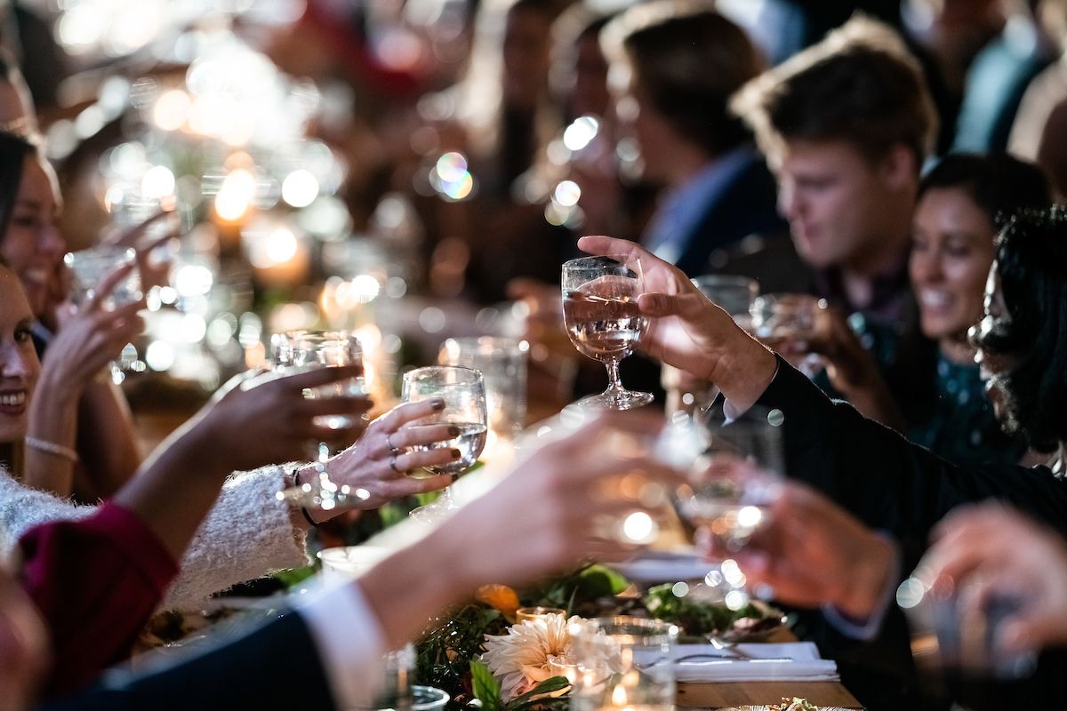 candid shot of wedding guests toasting each other during speeches at a wedding reception in the isham family farm event barn