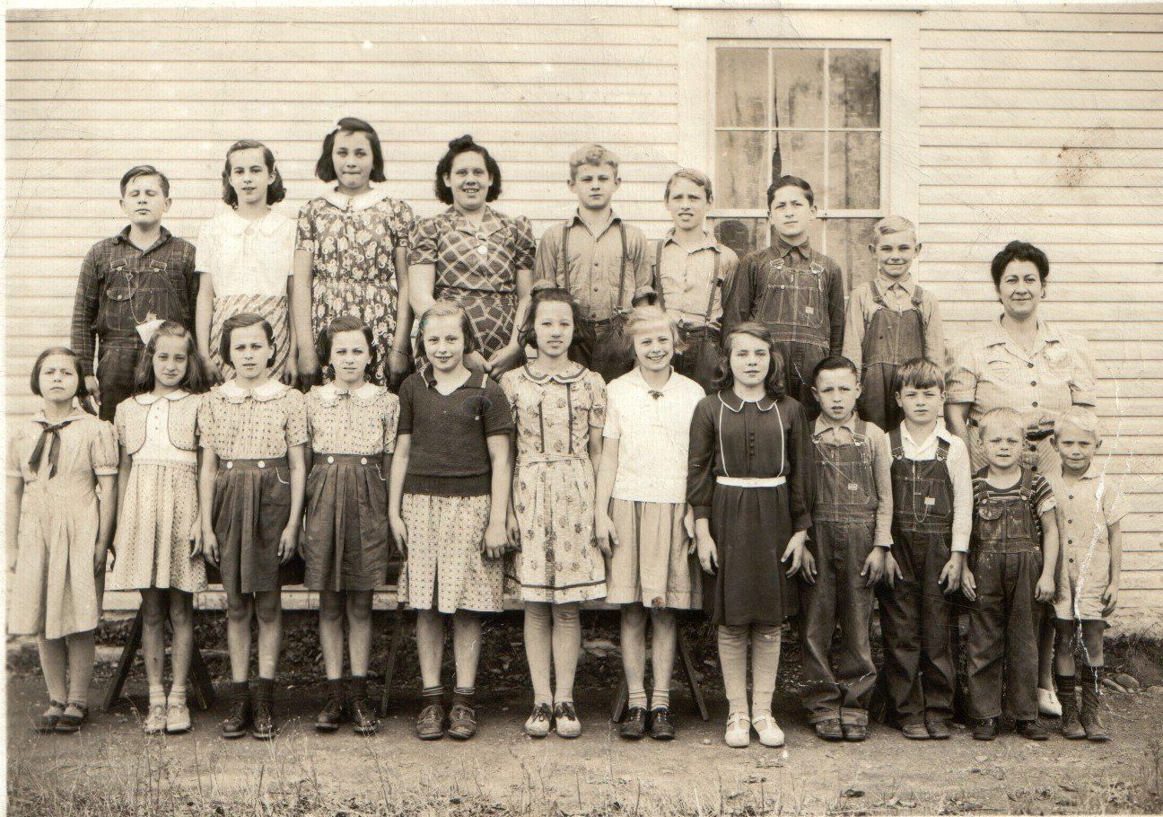 A historic photo of a group of children and adults, possibly relatives, standing in front of a house.
