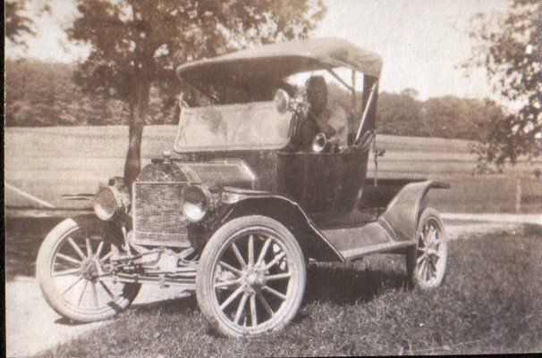 An old black-and-white photo of a vintage car, likely from the early 1900s, with a person seated inside at Isham Family Farm