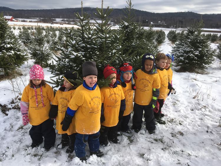 Group of school children gathered in front of snow covered evergreen christmas trees at isham family far christmas tree farm