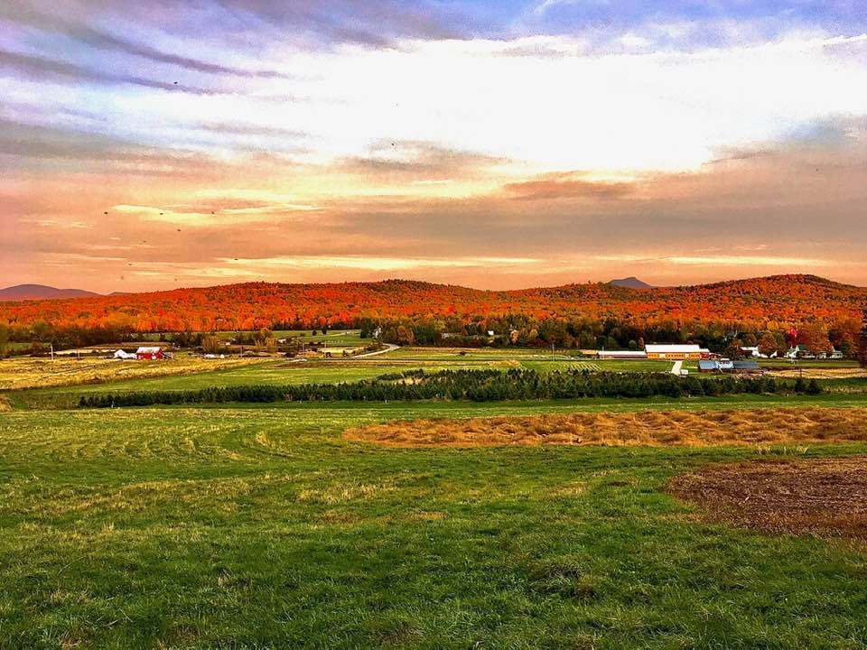 A breathtaking fall sunset over Isham Family Farm, with vibrant foliage on the hills and fields stretching below.