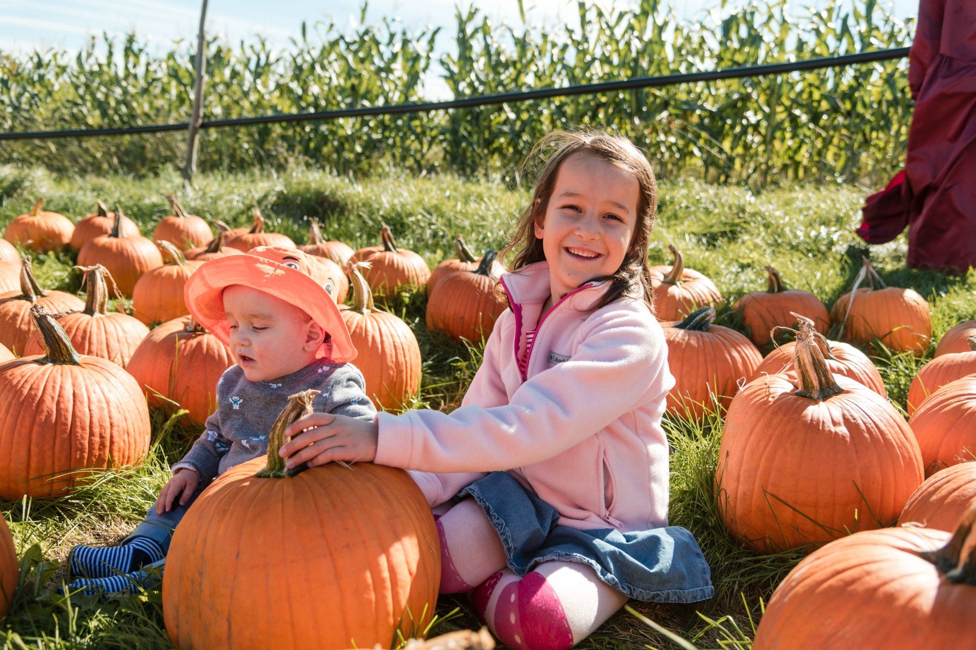 two young children smiling and sitting amongst the pumpkins in the isham family farm pumpkin patch.