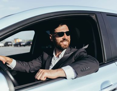 Man in sunglasses driving a light blue car, seen through the open window