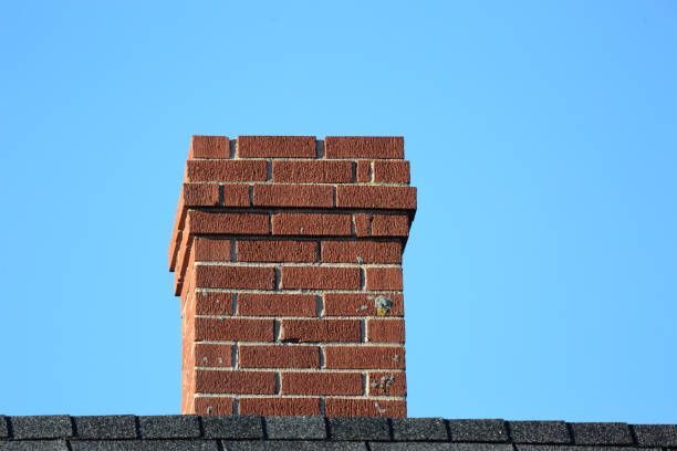 A brick chimney on top of a roof with a blue sky in the background.