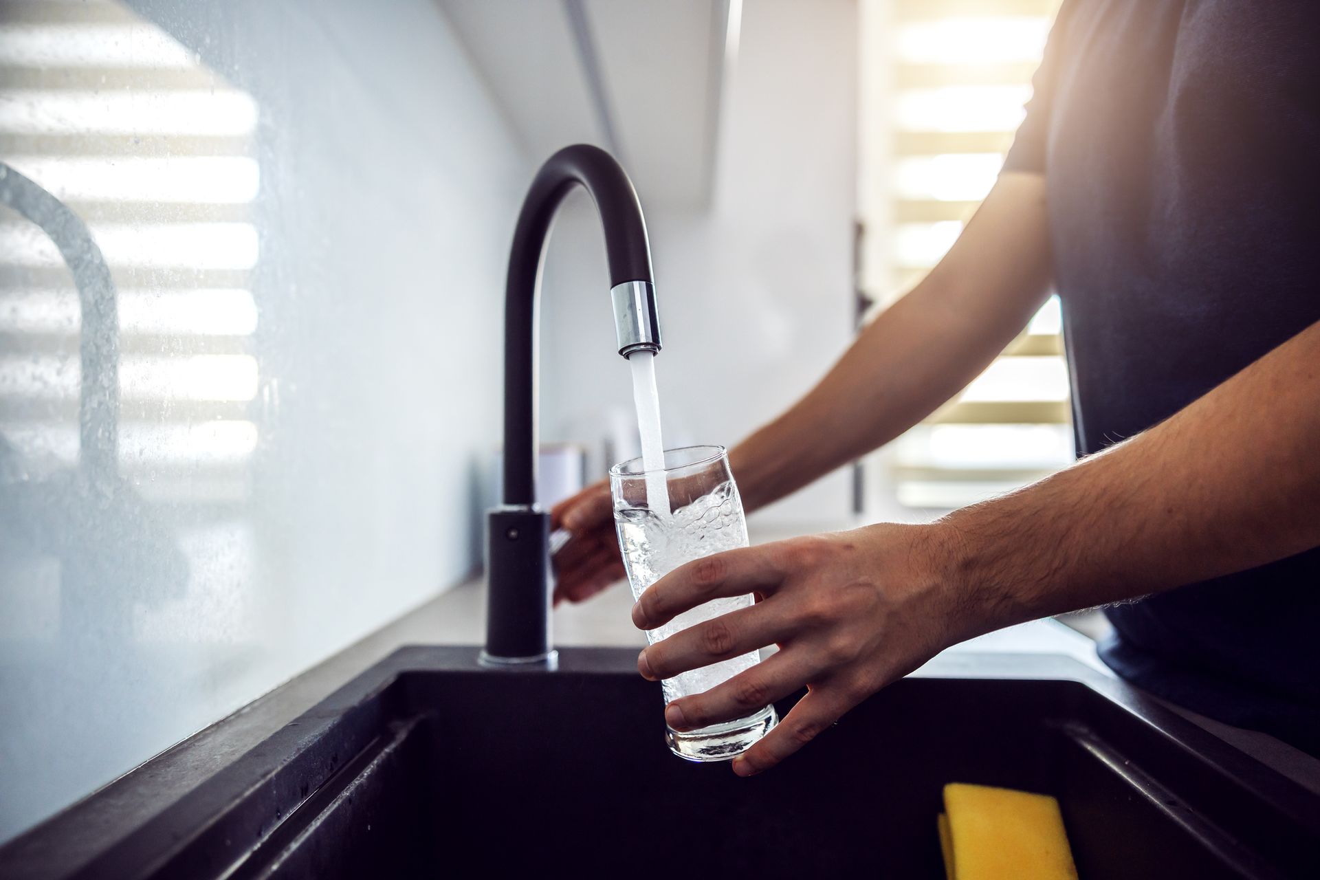 Close up of young man pouring fresh water from kitchen sink.
