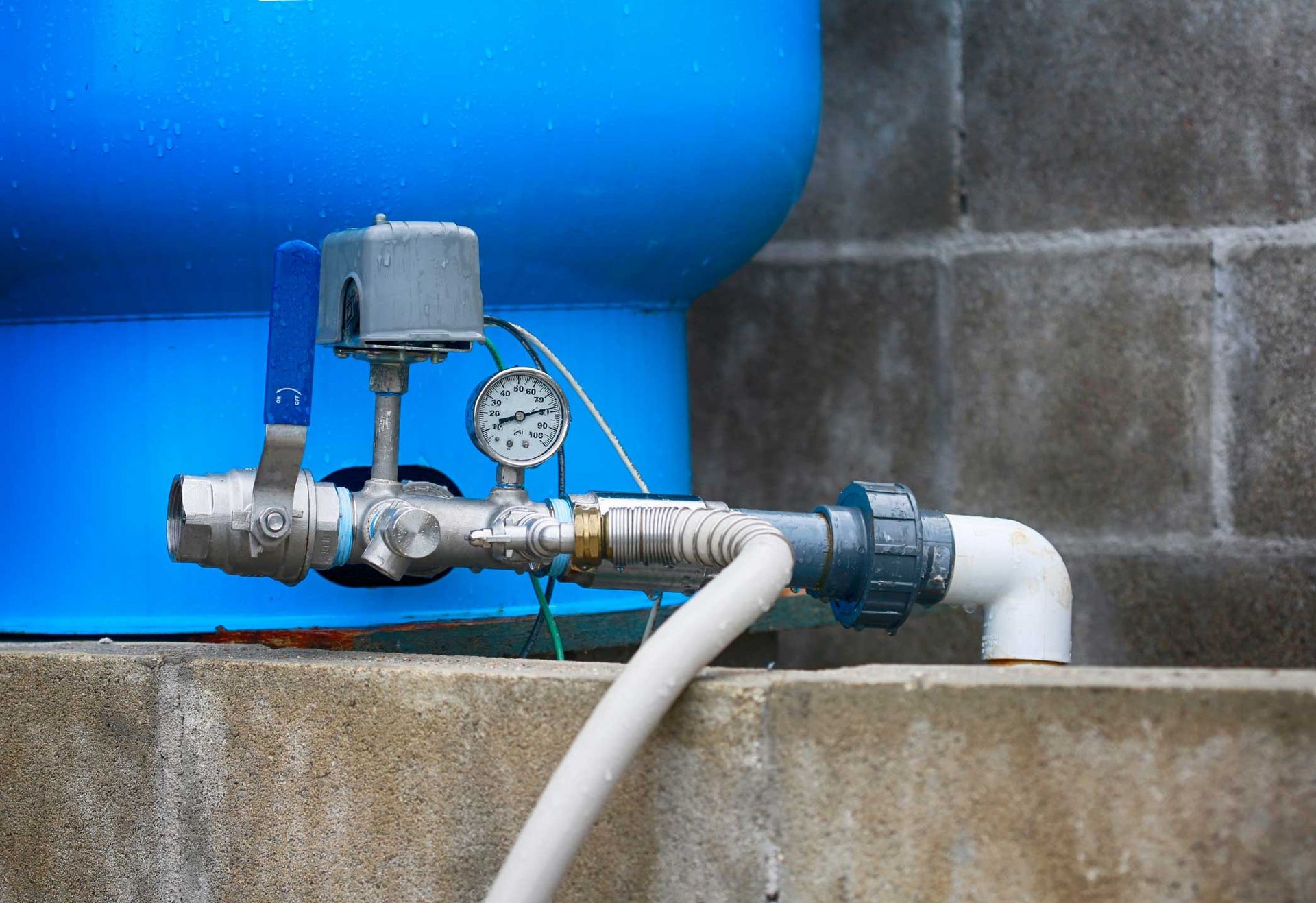 Water pressure gauge in front of a blue water well, representing home well drilling services.