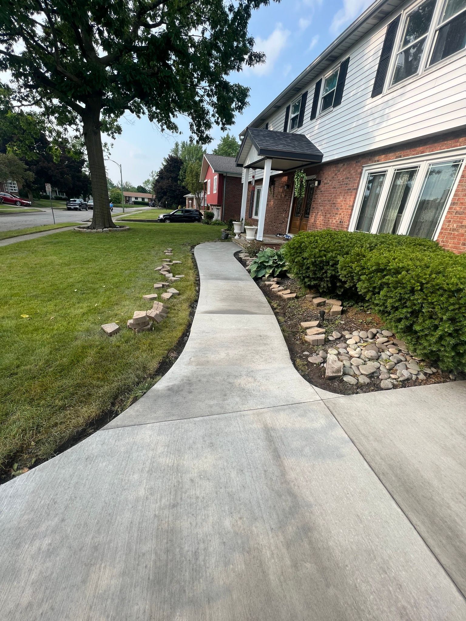 A concrete sidewalk leads toward the front entrance of a two-story brick and white-sided house on a sunny day.