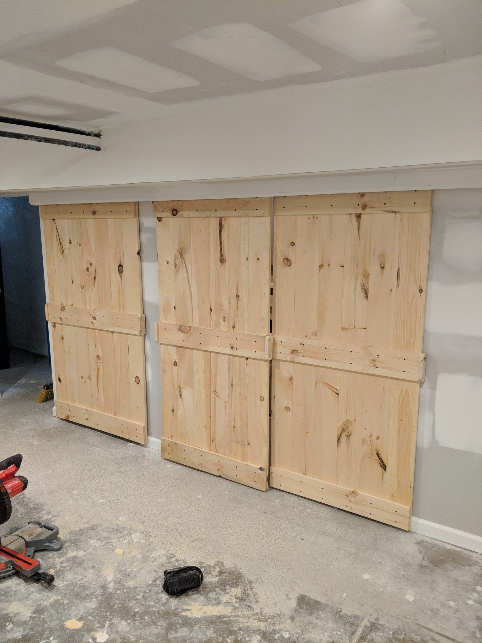 Four unfinished, wooden barn doors on a concrete floor, in a room under construction.