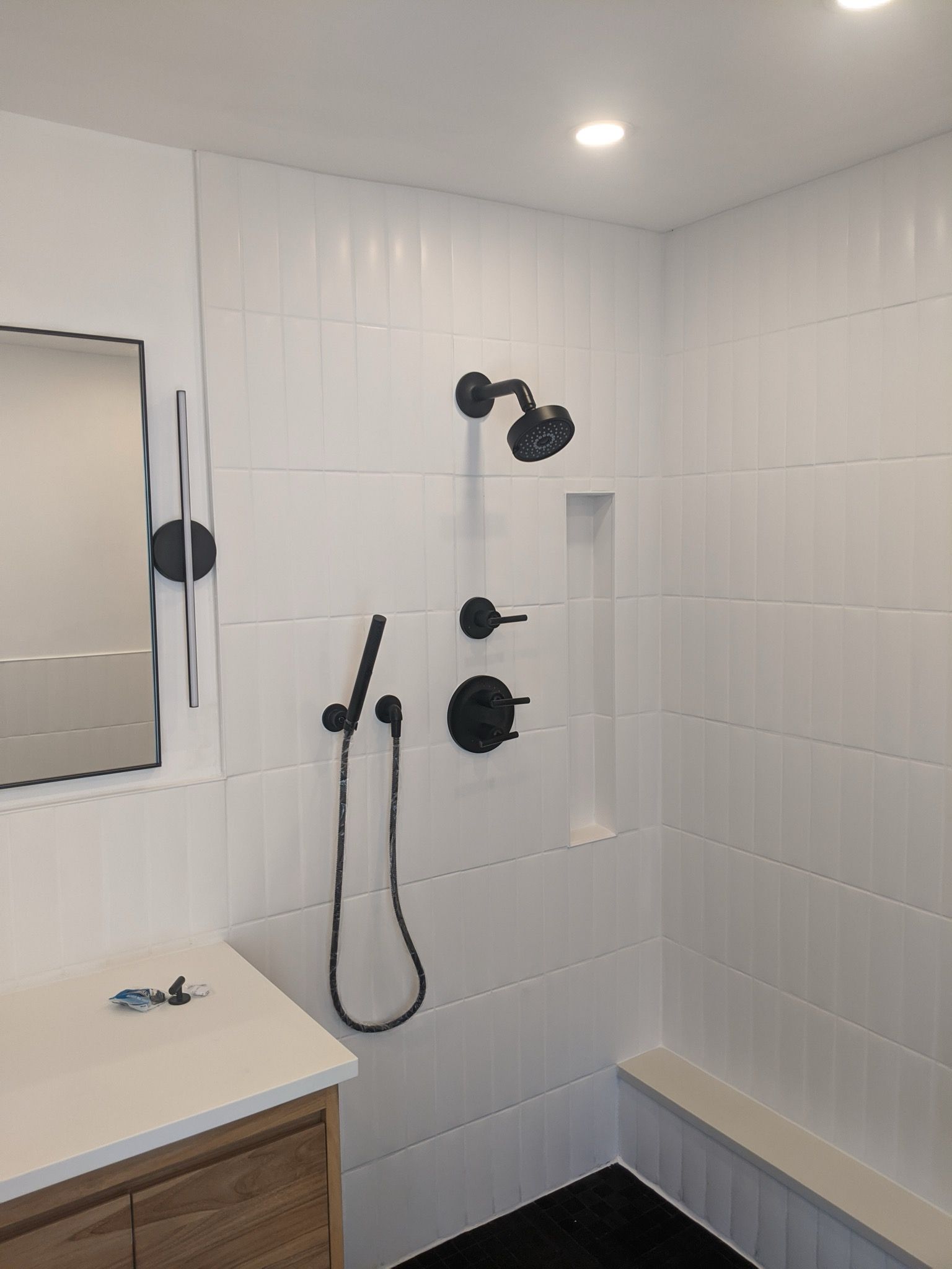 Modern bathroom with white tiled shower, black fixtures, and wooden vanity.