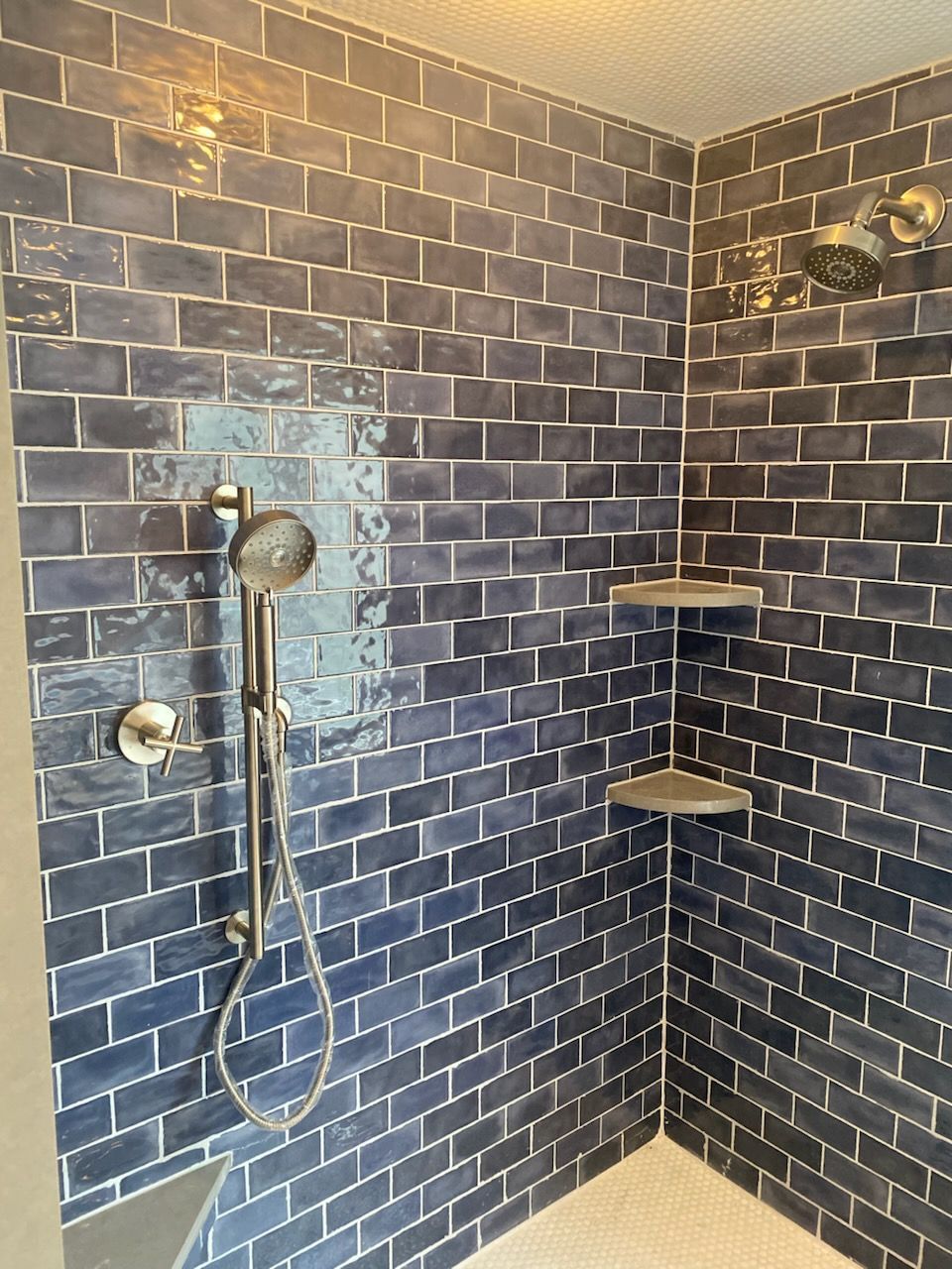 Blue tiled shower with silver fixtures and corner shelves.
