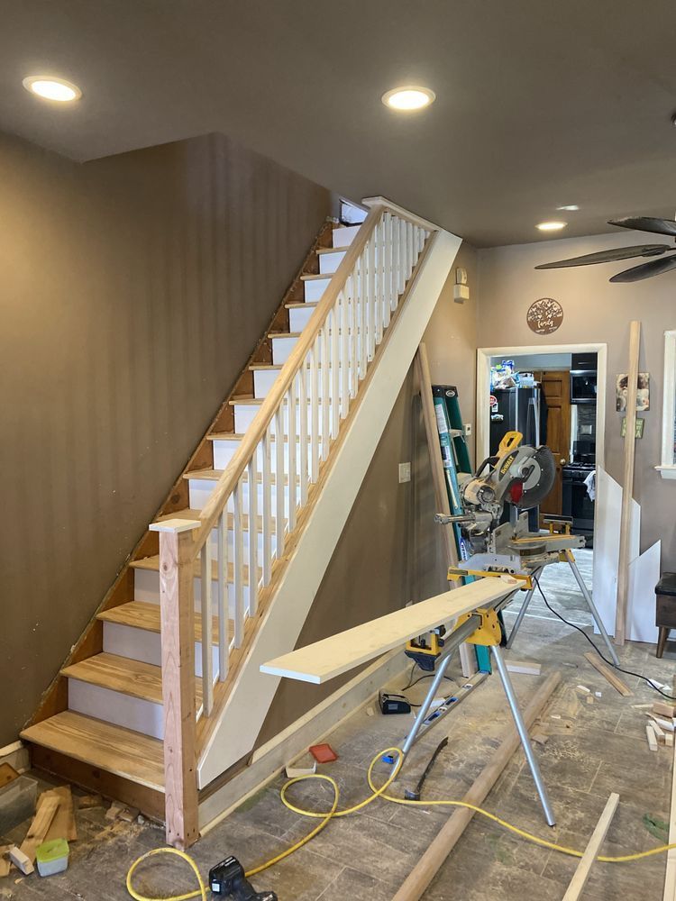 Staircase under construction inside a home. Wooden stairs, white railing, tools, and materials scattered about.
