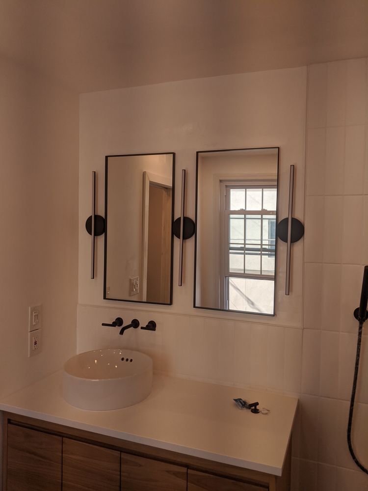 Modern bathroom with dual mirrors, round sink, and black fixtures against white walls.