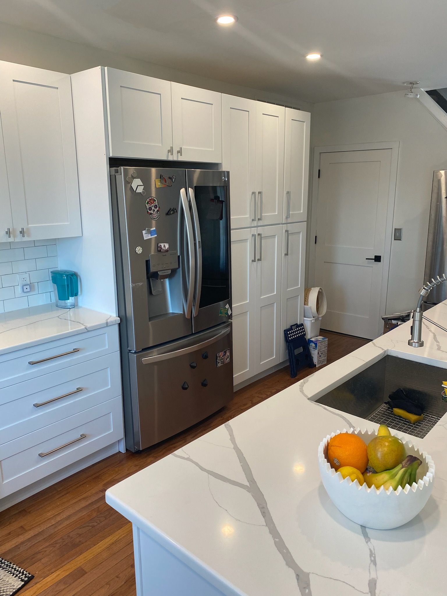 Modern white kitchen with stainless steel refrigerator and marble countertop island.
