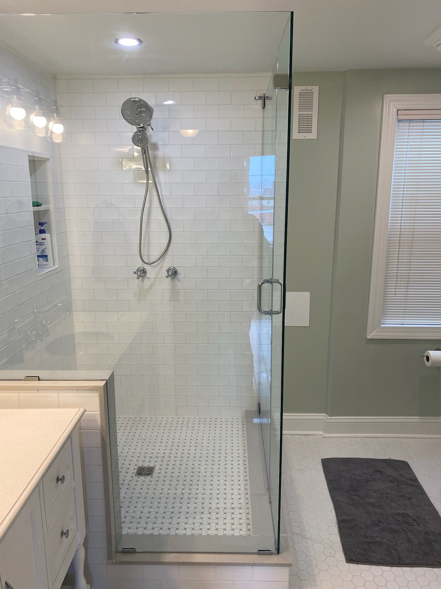 A modern bathroom with a glass shower enclosure, white subway tiles, and a mint-green wall.