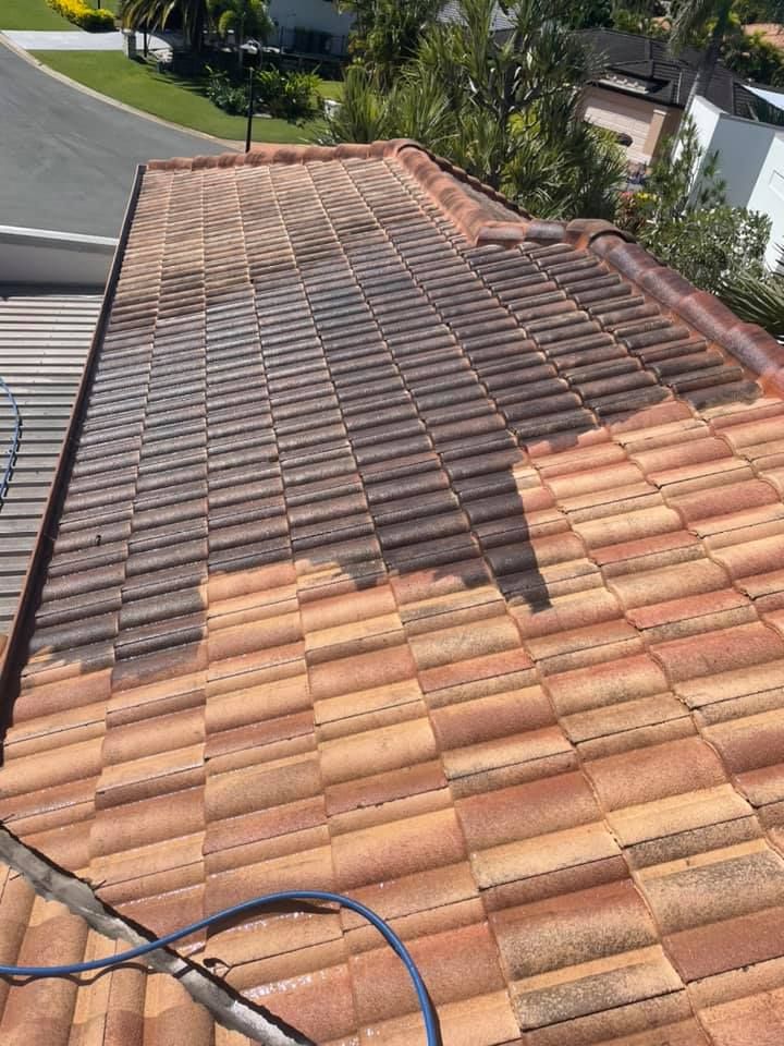A terracotta tile roof partially cleaned, showing a contrast between the dirty and clean areas, outdoors.