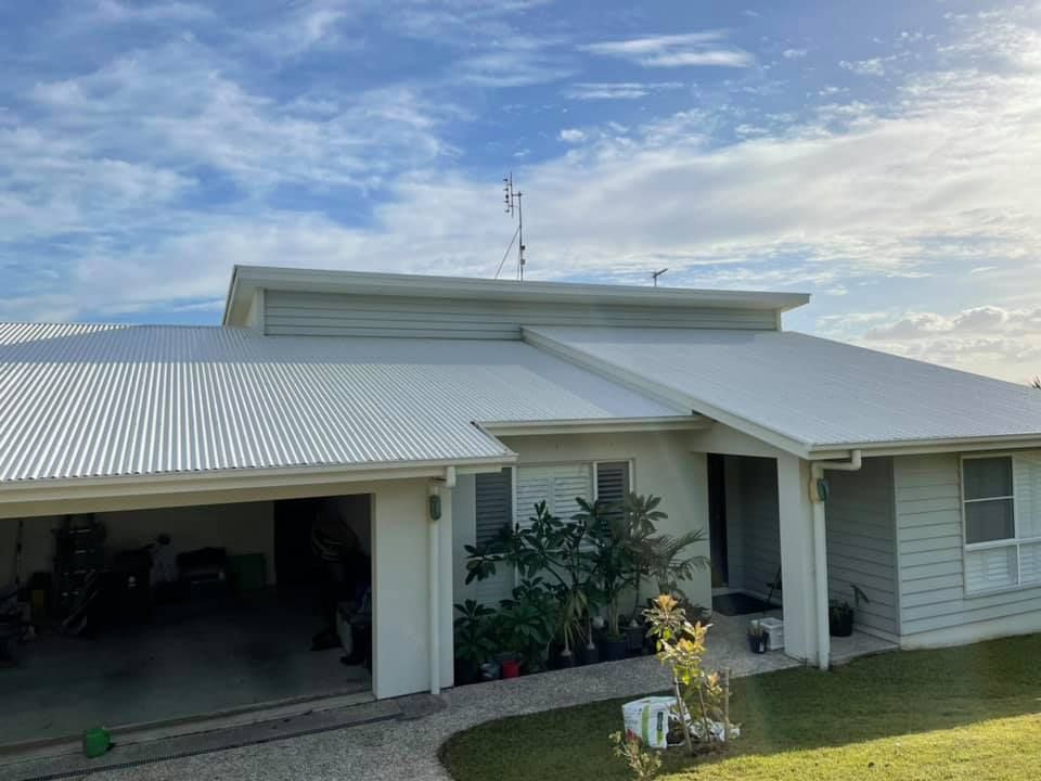 A white house with a corrugated metal roof, garage, and a cloudy sky background.