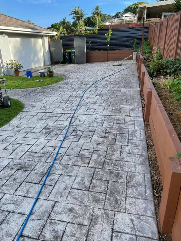 Stamped concrete driveway with a blue hose running along it, beside a retaining wall.