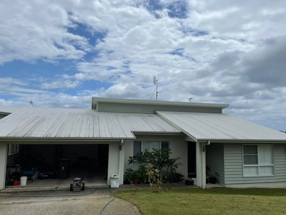 A light-colored house with a metal roof under a cloudy blue sky. A garage is on the left.