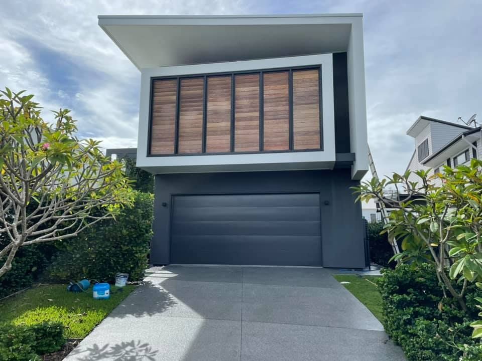 Modern two-story house with gray garage door, wooden shutters, and a concrete driveway.