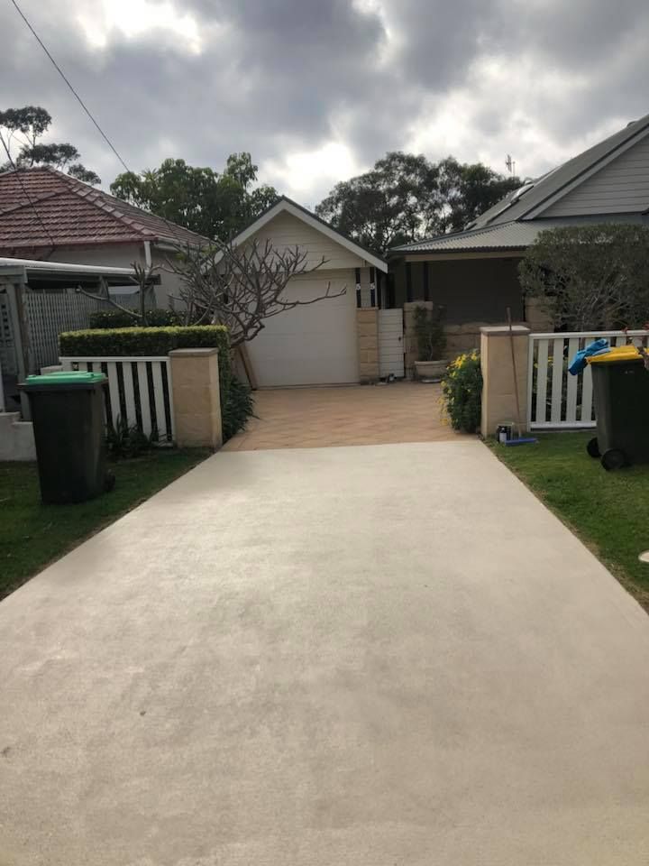 Driveway leading to a garage between two houses, overcast sky. Trash cans line the driveway.
