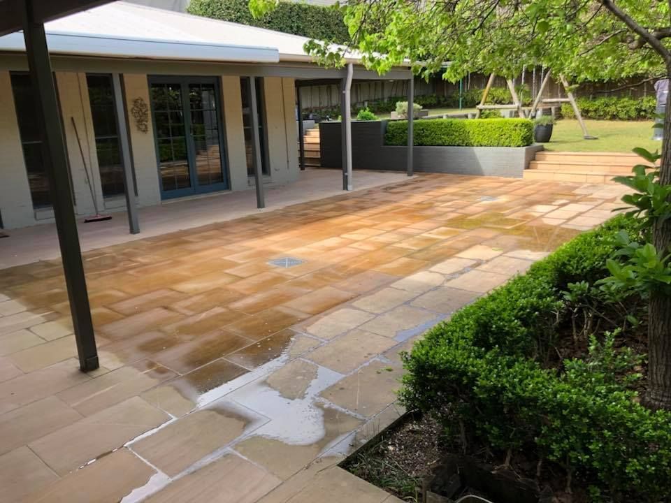 Patio with sandstone pavers, adjacent to building, hedge, and greenery.