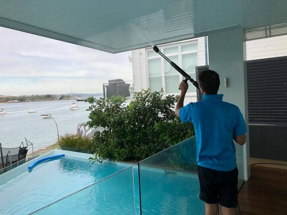 Person cleaning a ceiling with a long-handled tool, overlooking a pool and harbor.