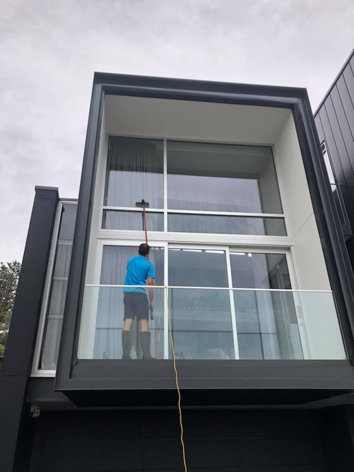 Person cleaning a large window with a long-handled brush on a modern building.