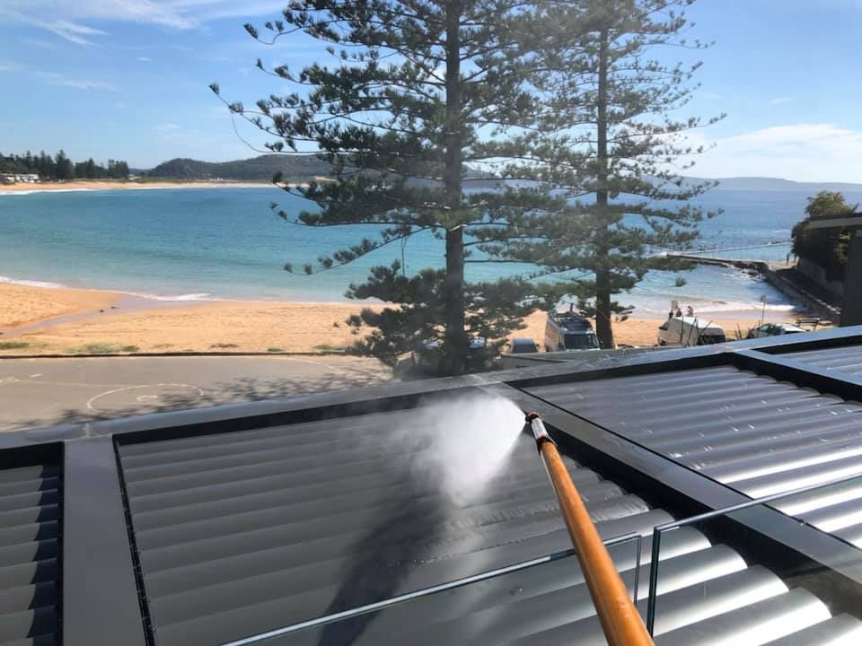 Pressure washing a black corrugated roof with a beach and ocean view in the background.