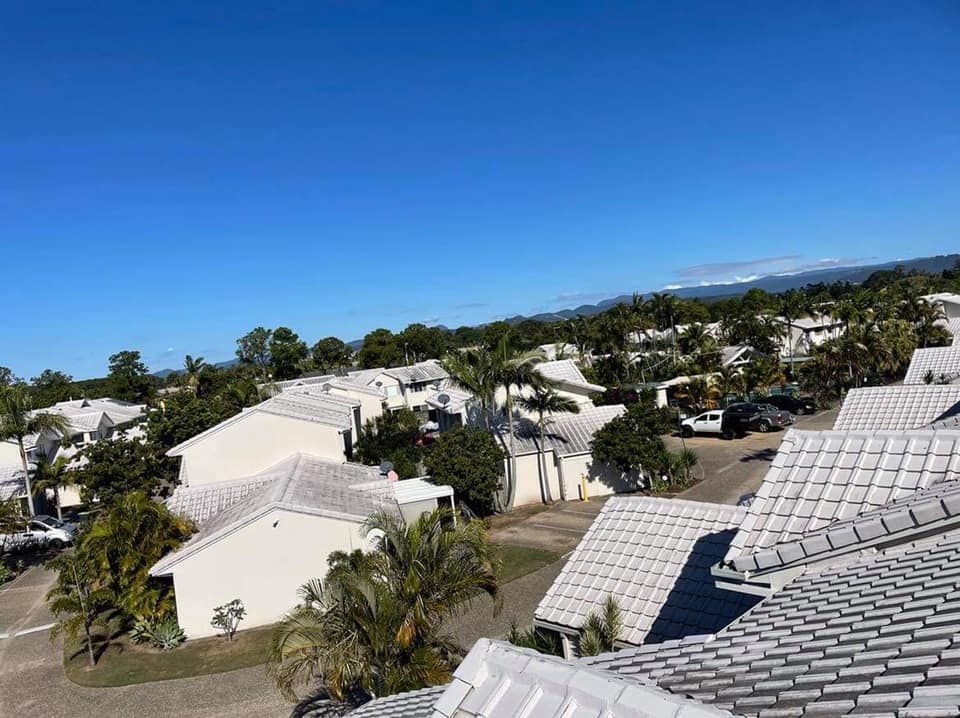 Overhead view of white buildings with tiled roofs under a blue sky, trees in between, mountains in the distance.