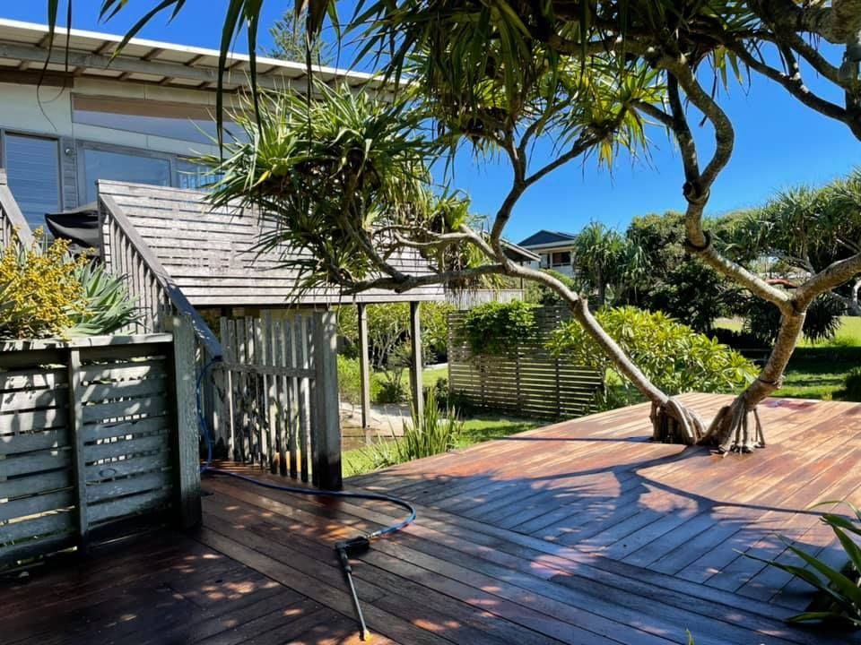 Wooden deck with tree growing through it, attached to a house with wooden siding. Bright blue sky.
