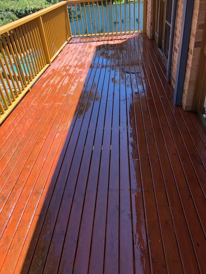 Wooden deck, freshly stained reddish-brown, with yellow railing and partial sunlight.