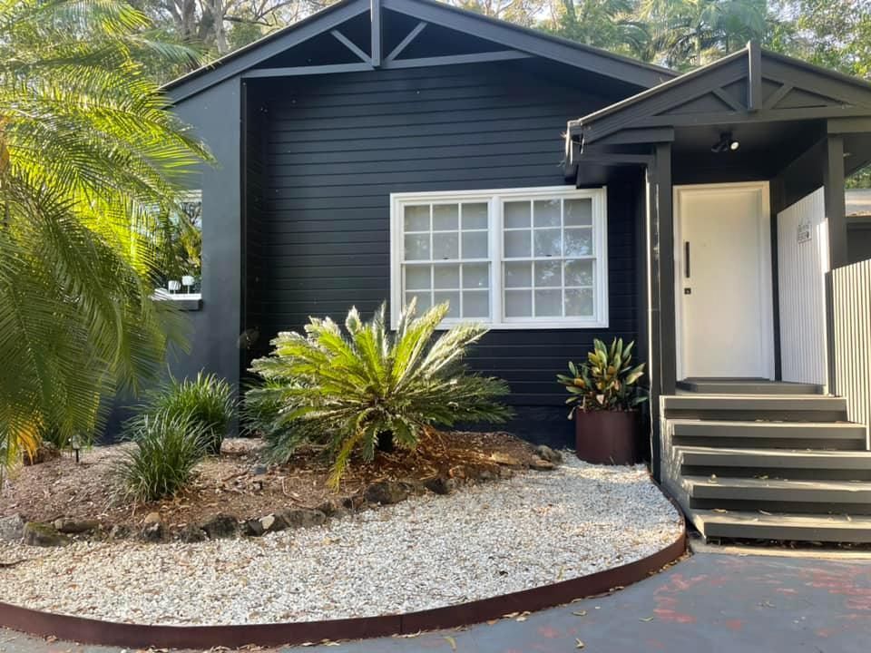 Black house with white-framed window and door. Gravel landscaping with green plants.