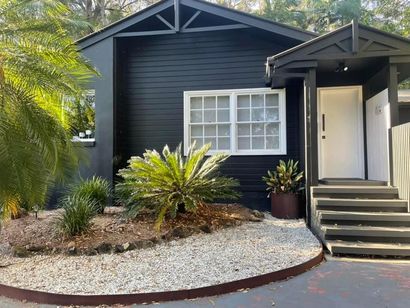 Black house with white-framed window and door. Gravel landscaping with green plants.