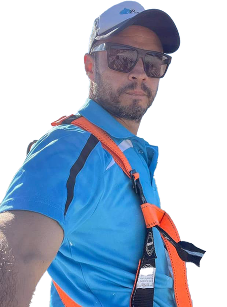 Man in blue shirt, sunglasses, and safety harness, looking at camera.