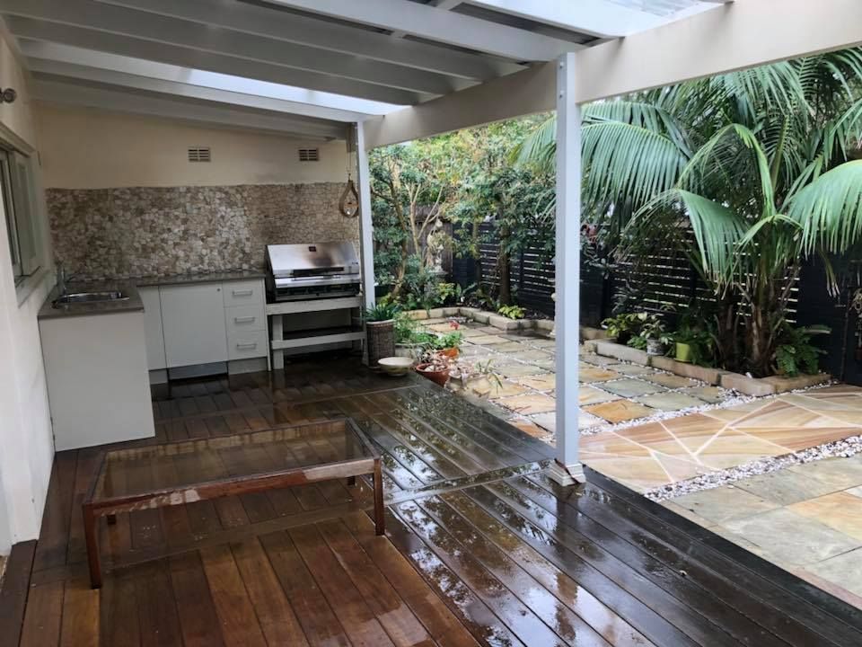 Covered outdoor kitchen with grill, wood deck, and garden view.